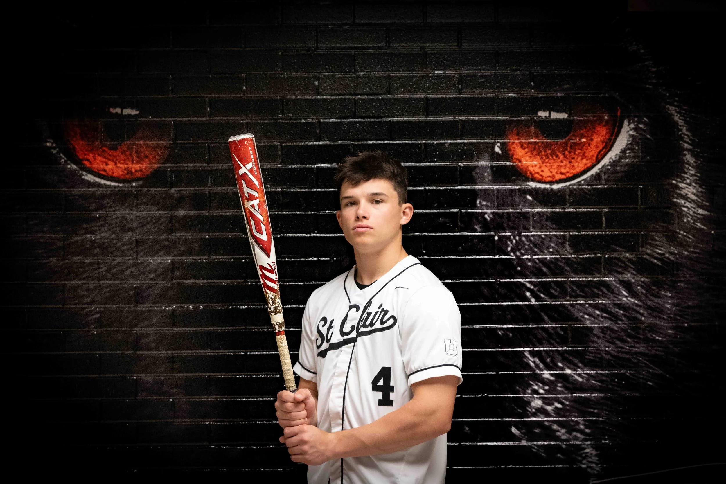 Class of 2026 Upper St. Clair senior Nico in baseball uniform holding a bat in front of tiger mural