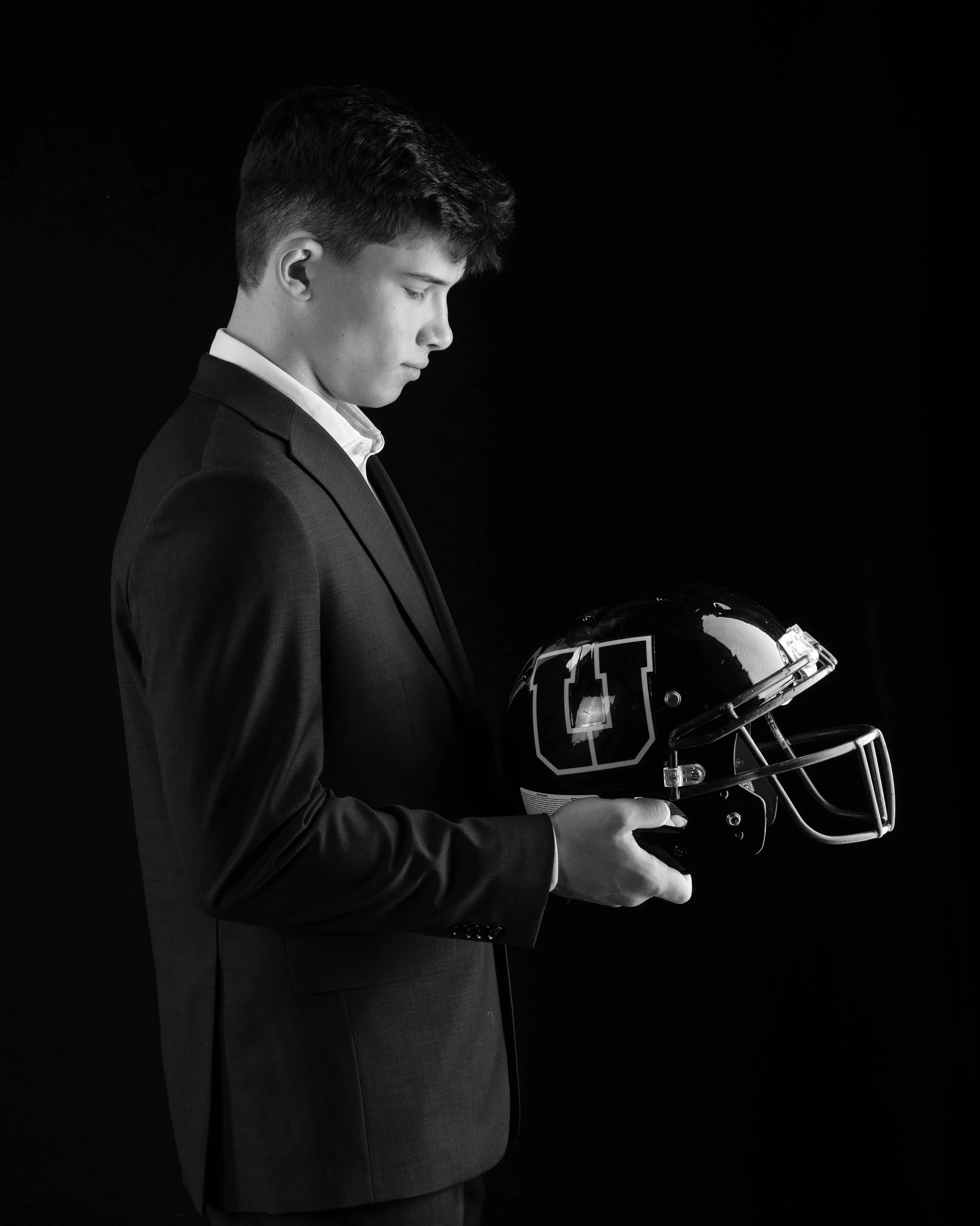 Class of 2026 Upper St. Clair senior Nico in a black suit holding a football helmet in studio portrait