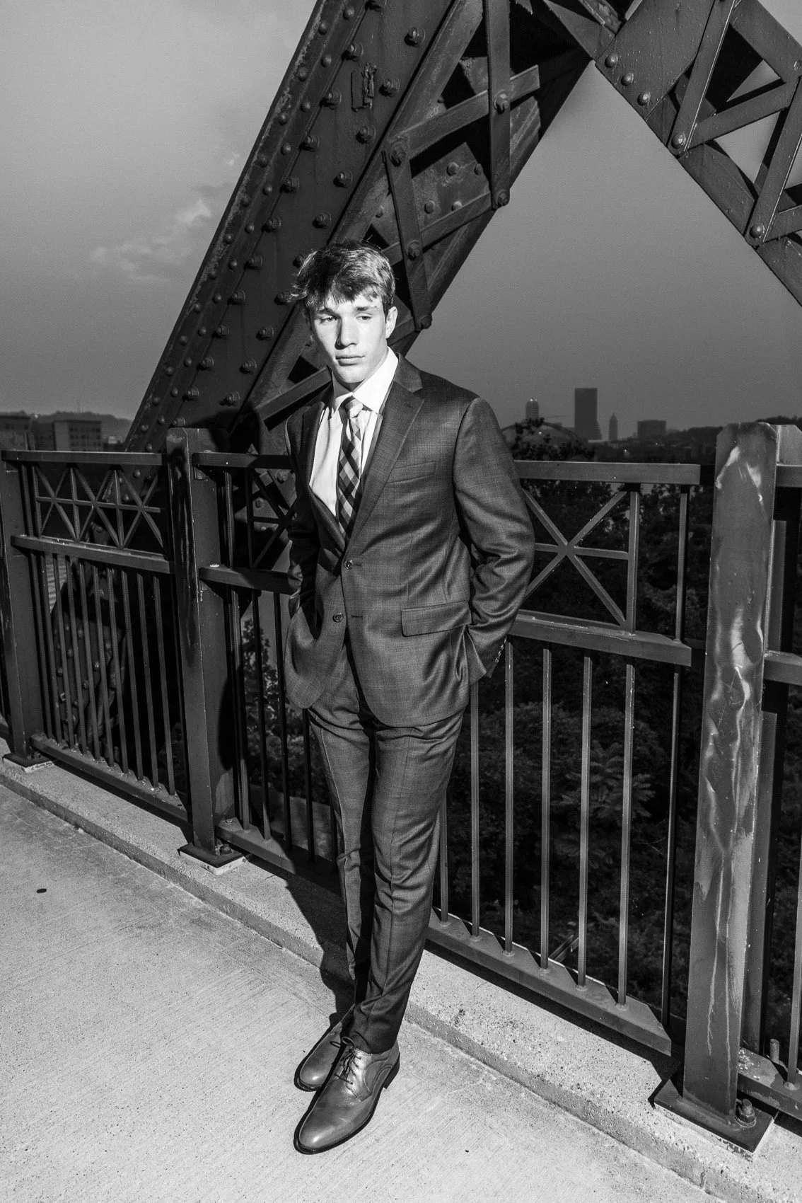 Senior Pictures Pittsburgh at Hot Metal Bridge. Young man in a dark suit posing on the iconic Hot Metal Bridge during golden hour for bold urban senior pictures with Pittsburgh skyline.