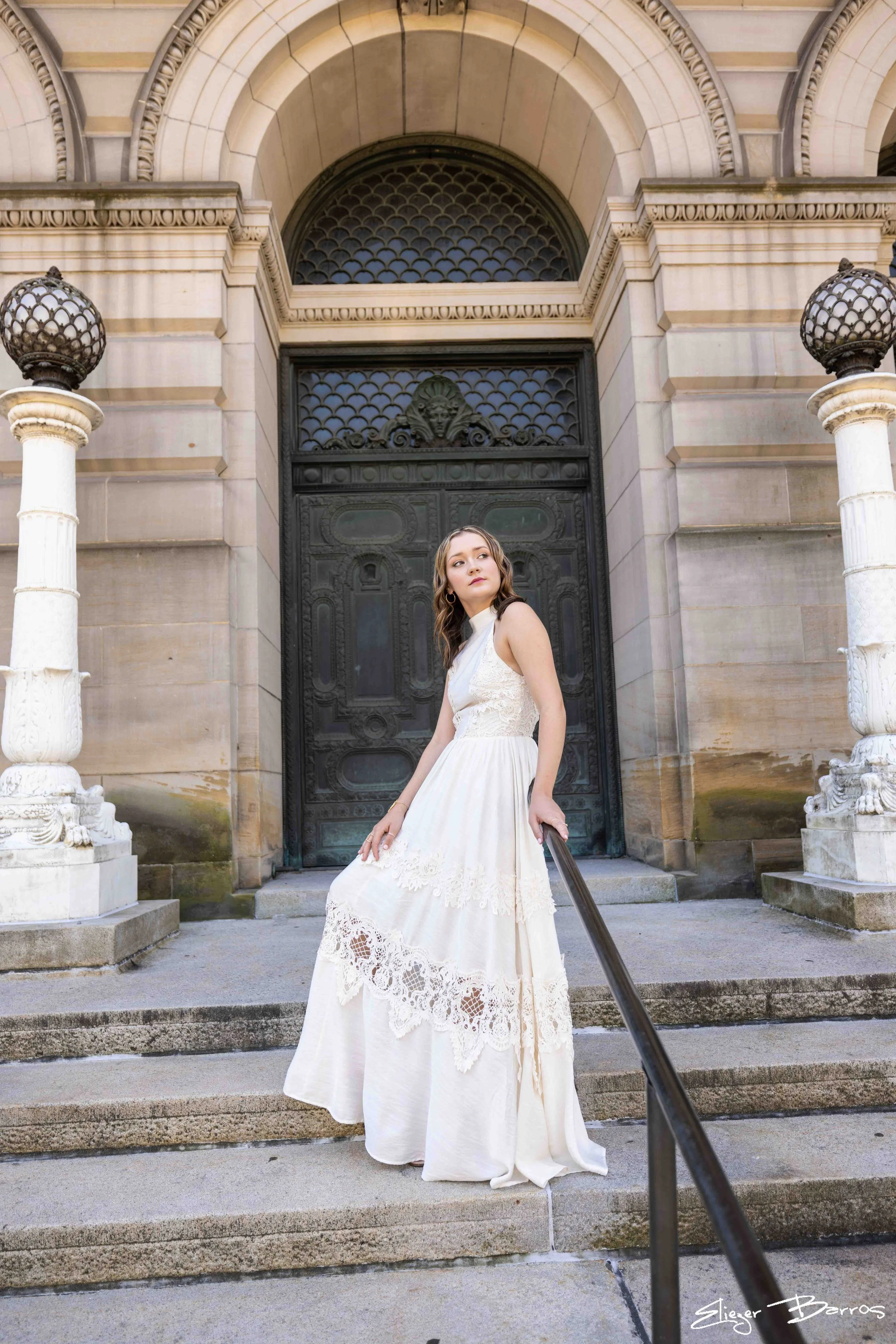 Senior Pictures Pittsburgh in Oakland at Mellon Institute. Young woman in a flowing white lace dress posing on grand stone steps in front of historic architecture for elegant academic senior portraits.