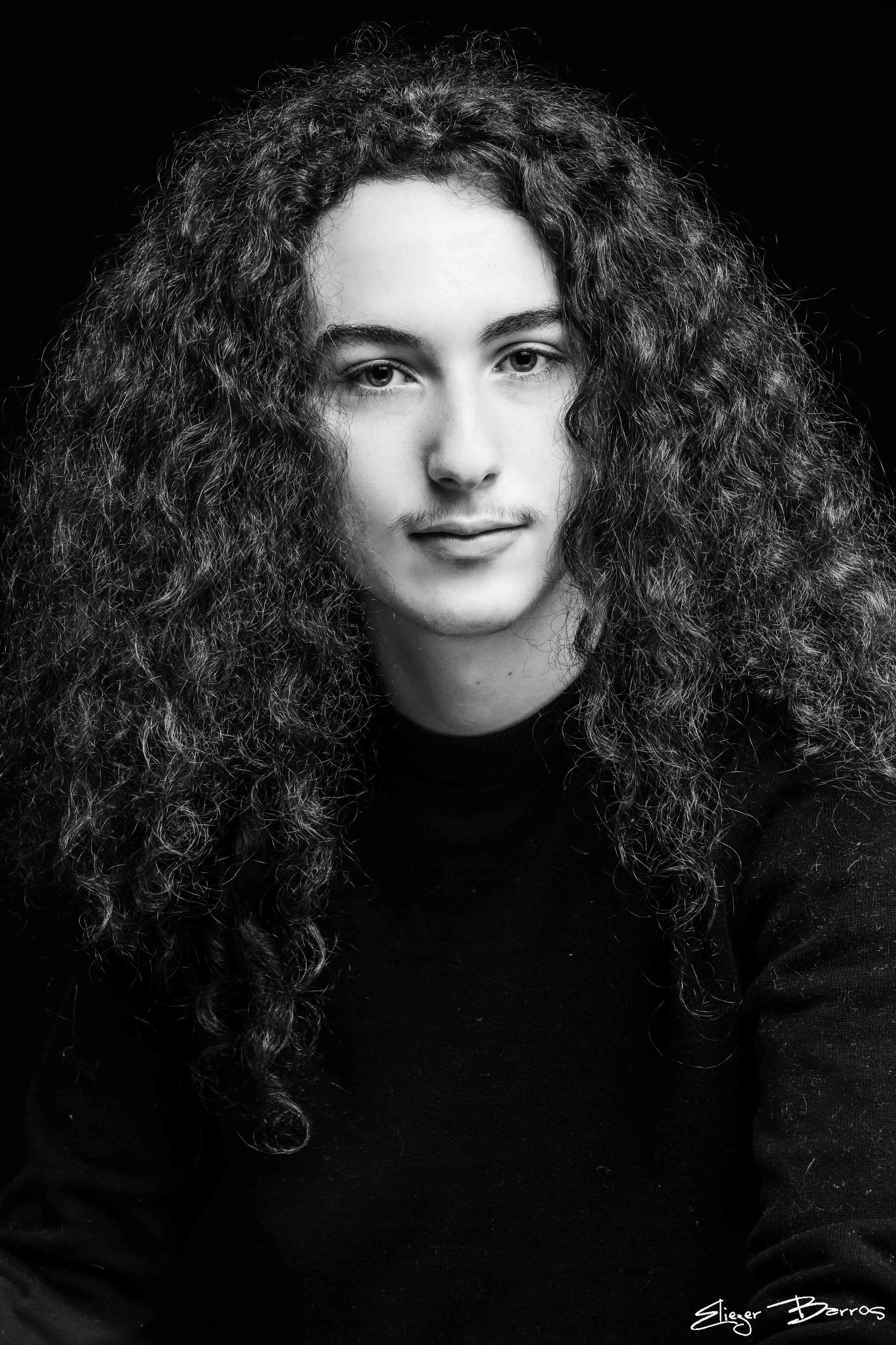 Black and white portrait of a woman with long curly hair, wearing a dark top, looking directly at the camera with a neutral expression.