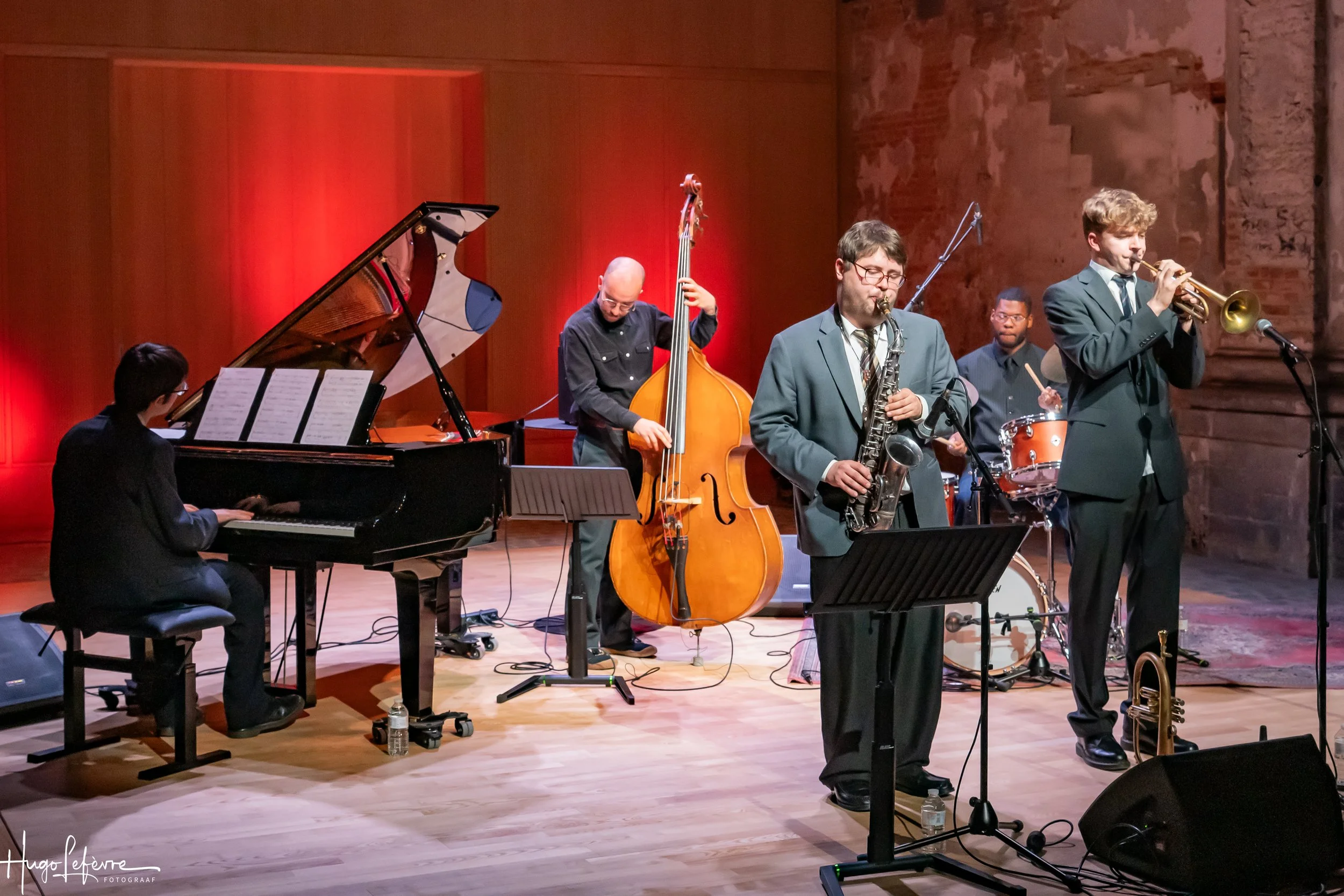 Jazz band performing on stage: pianist, double bassist, saxophonist, trumpeter, and drummer.