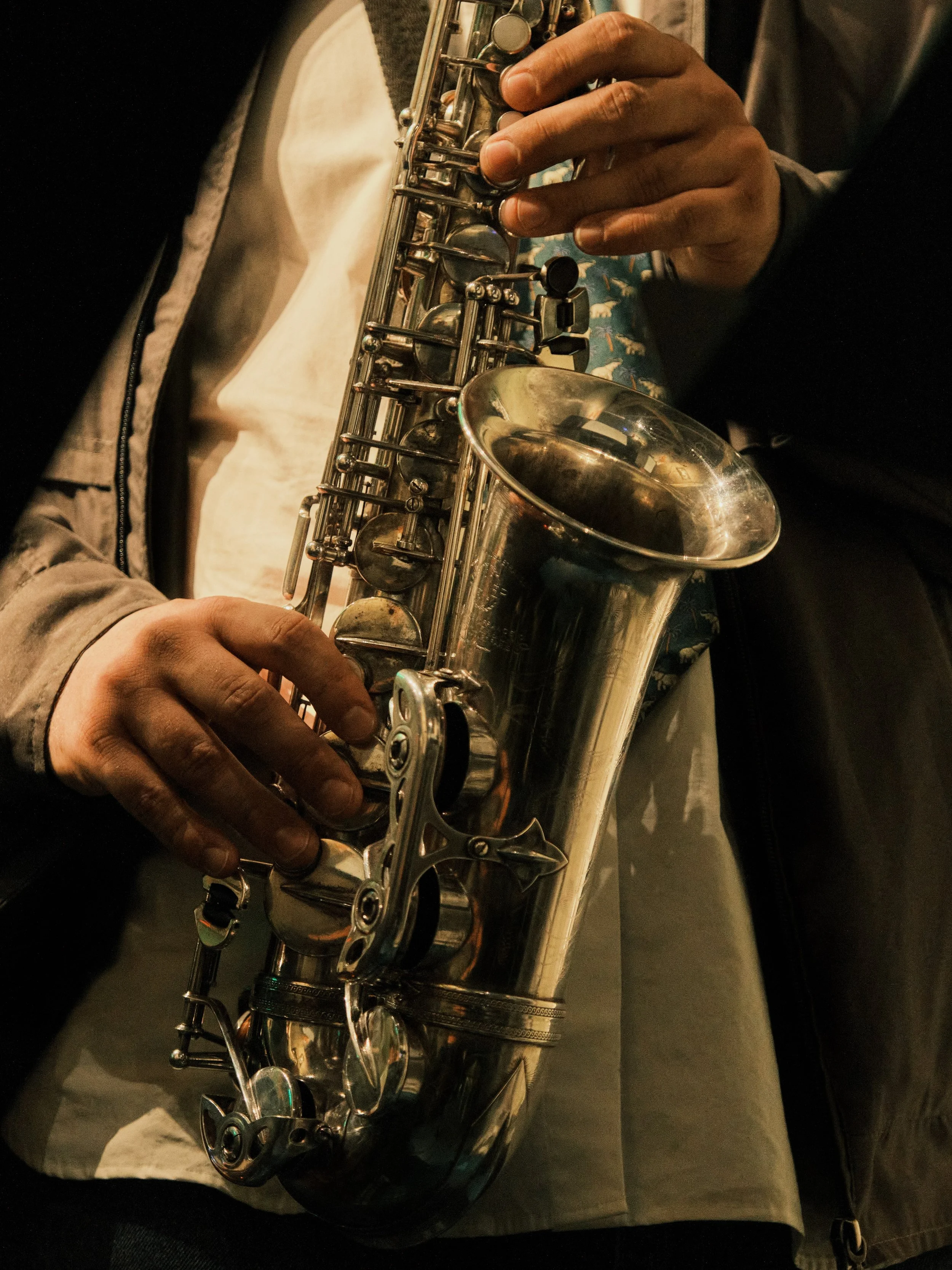 Close-up of a person playing a silver saxophone, focusing on their hands and the instrument.