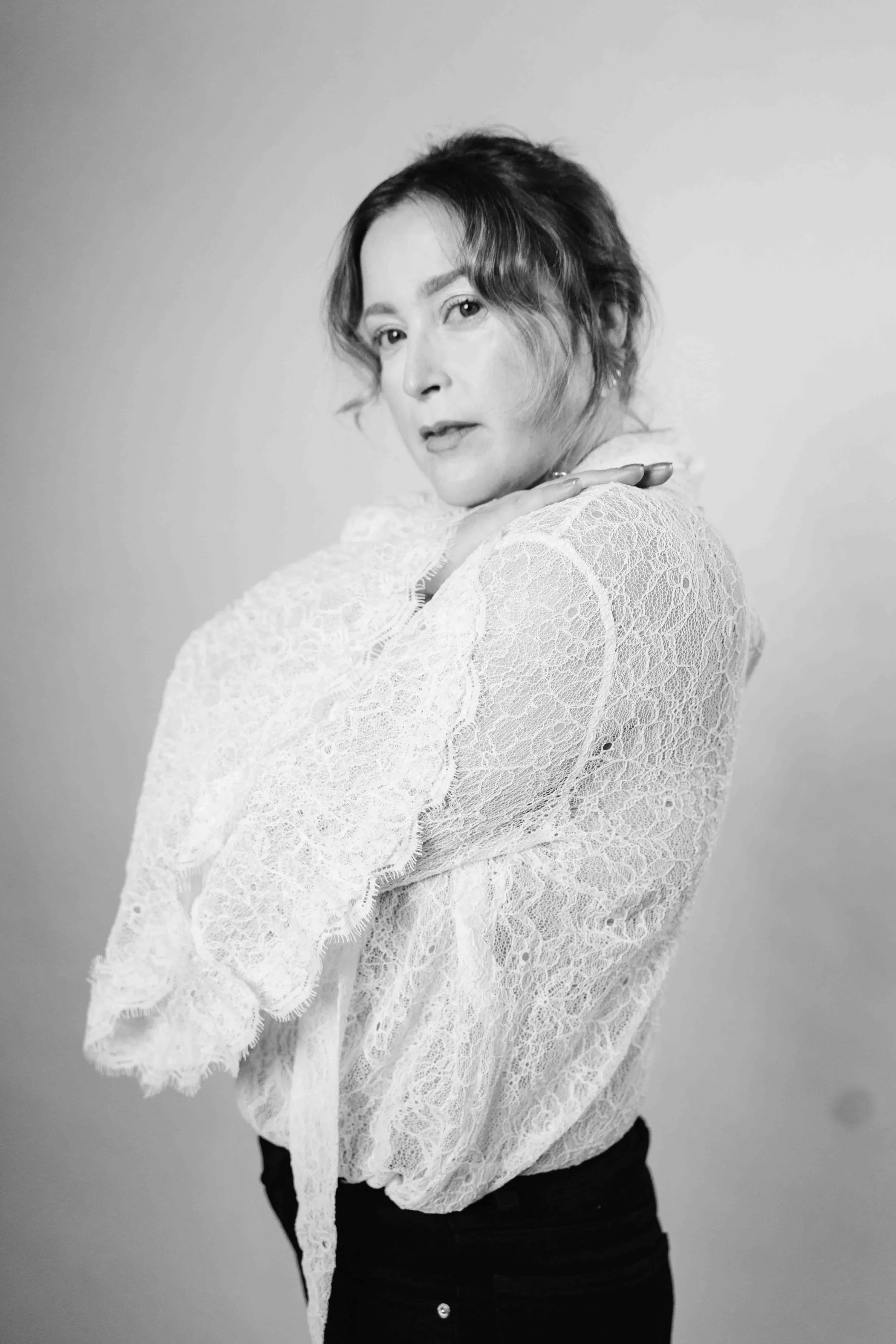 Black and white portrait of a woman with short wavy hair, wearing a lace blouse, looking at the camera with a confident expression, against a plain backdrop.