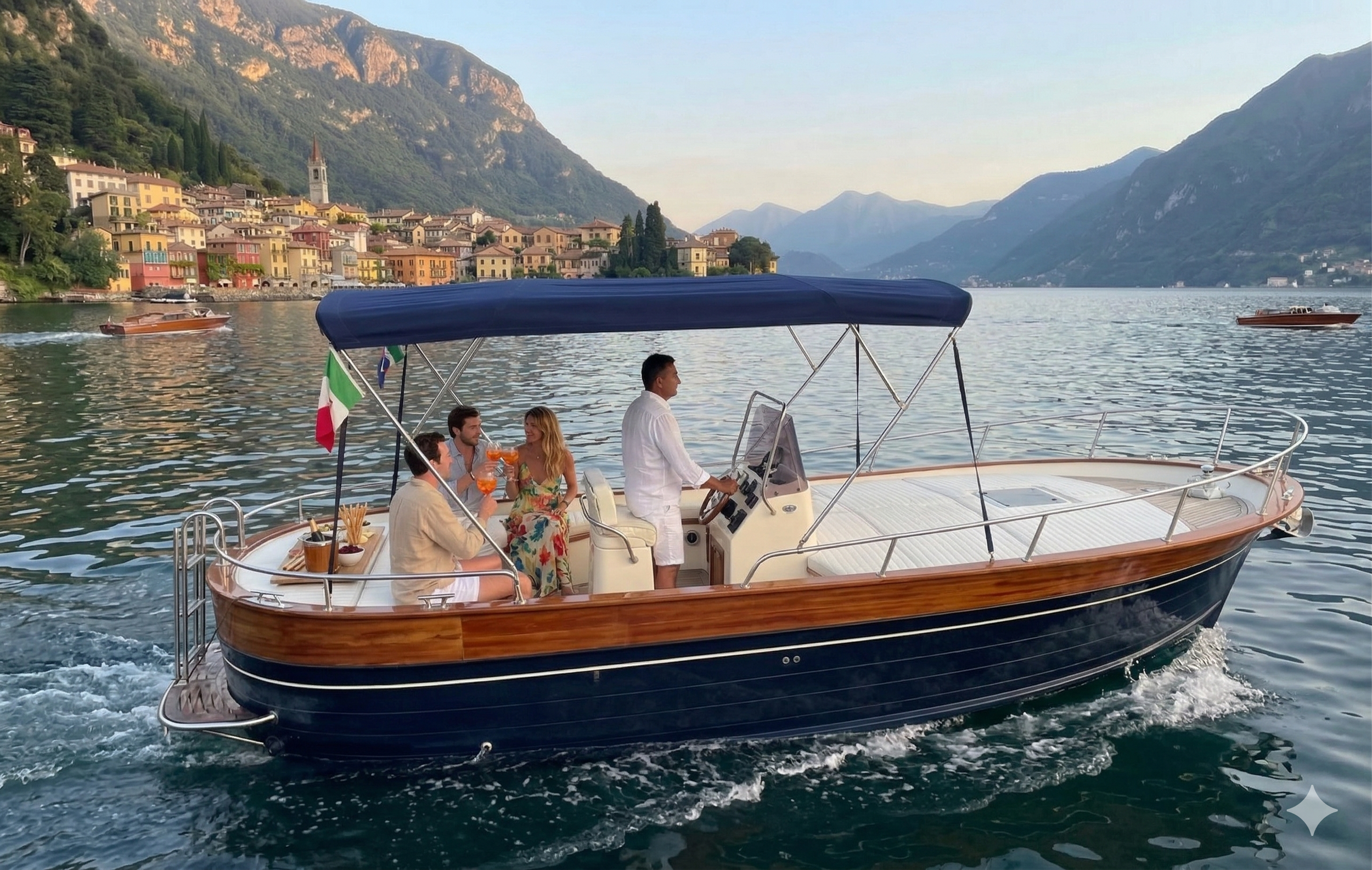 Four people enjoying drinks on a small yacht sailing on a lake surrounded by mountains and colorful houses.