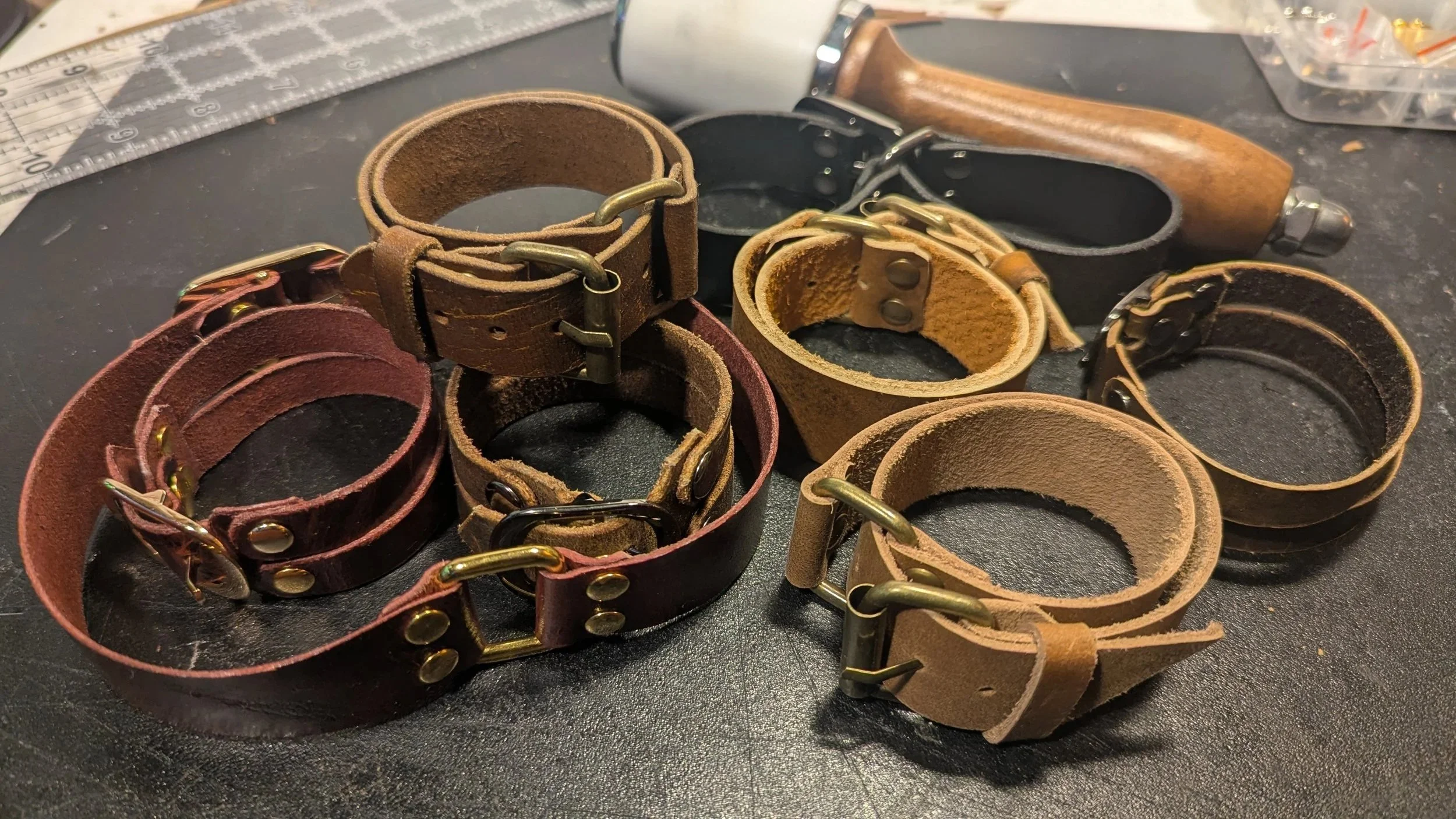 Multiple leather bracelets with metal hardware on a work table.