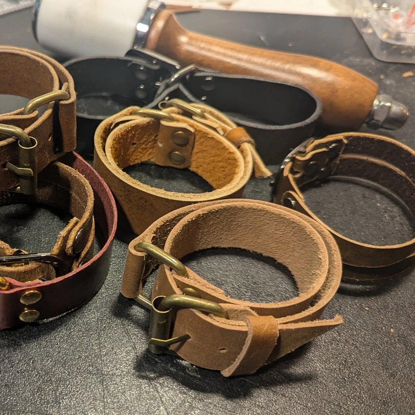 Various leather bracelets and handcuffs with metal buckles and rings lying on a black surface.