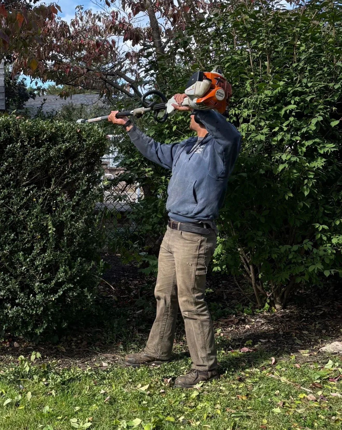 A person in outdoor clothing using a leaf blower to blow leaves in a garden or yard.