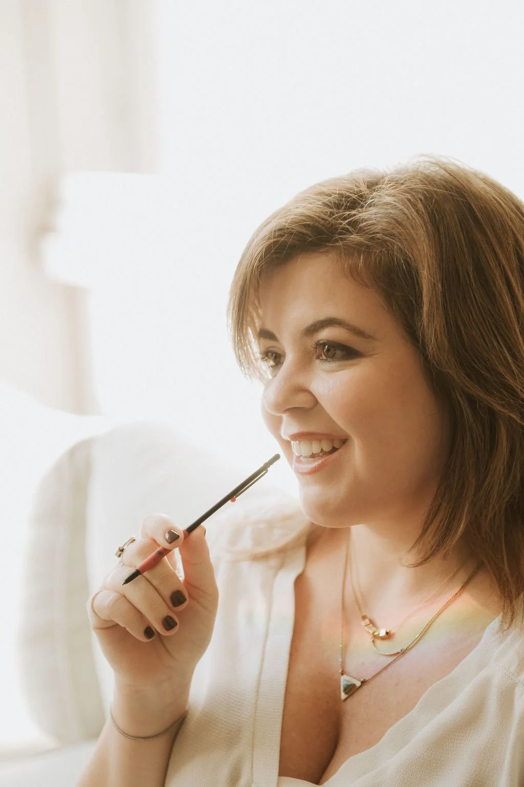 A smiling woman with short auburn hair holding a pen near her face