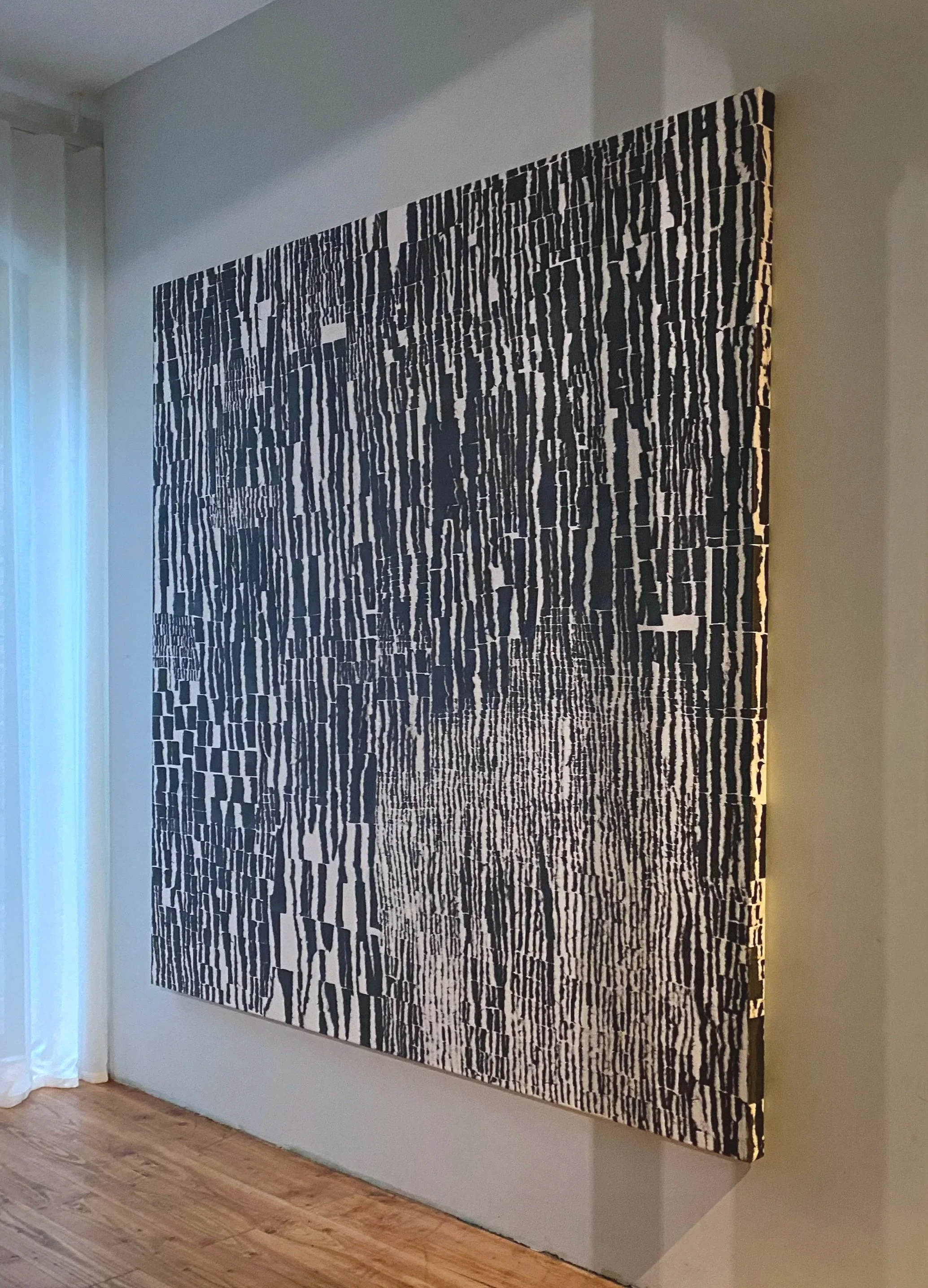 Large black and white abstract patterned artwork on a wall in a room with light-colored walls and hardwood flooring.