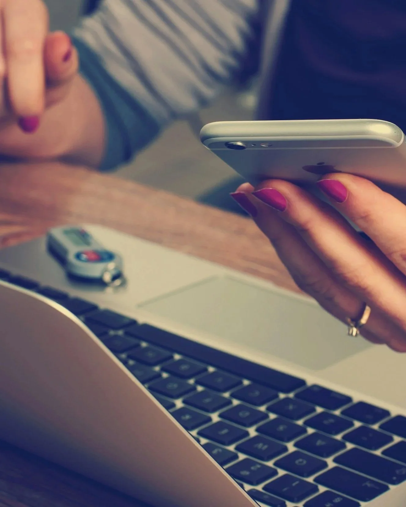 Person holding a smartphone over a laptop with a car key on the desk.