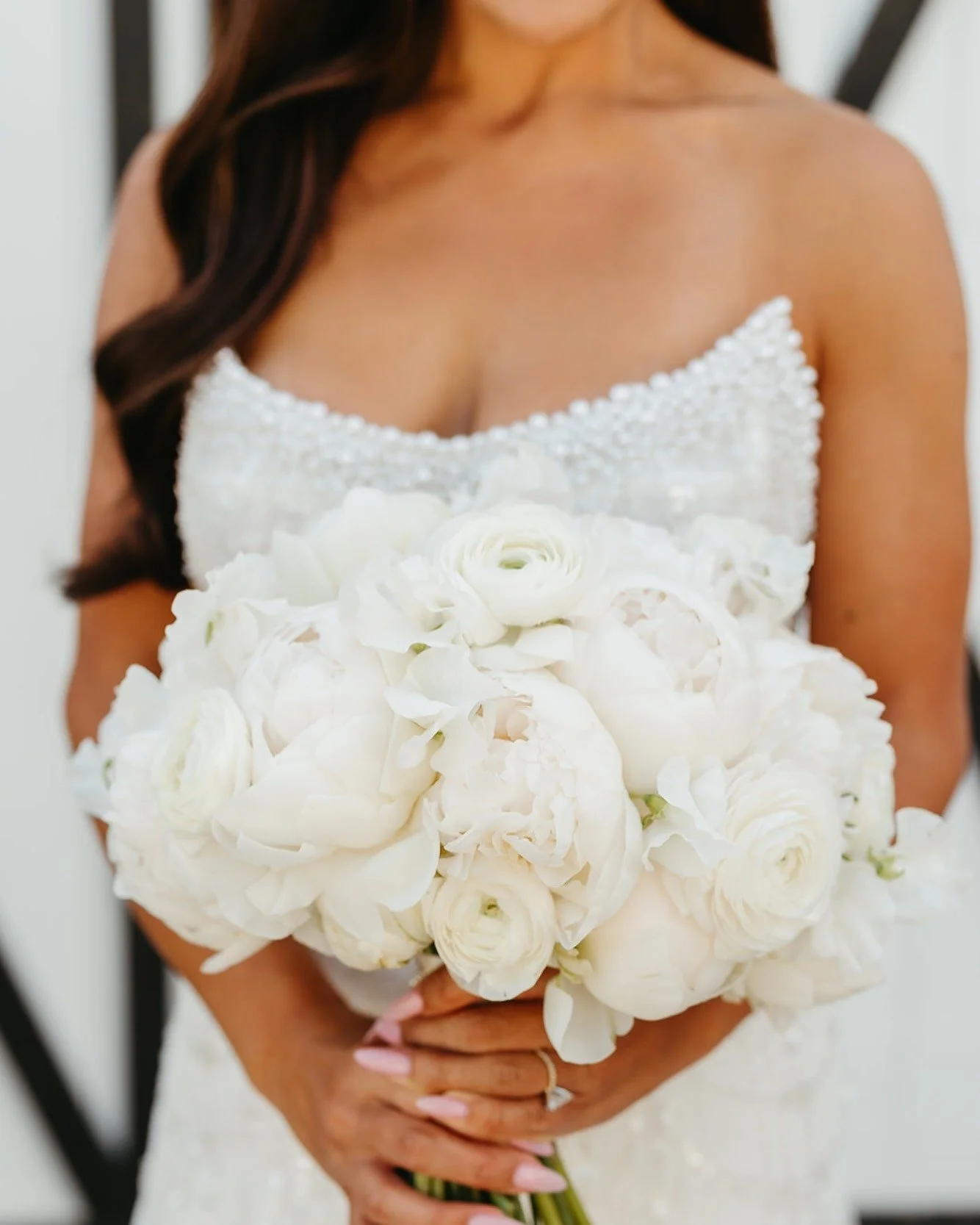 A woman holding a bouquet of white flowers, wearing a strapless white dress with beaded embellishments on the top.