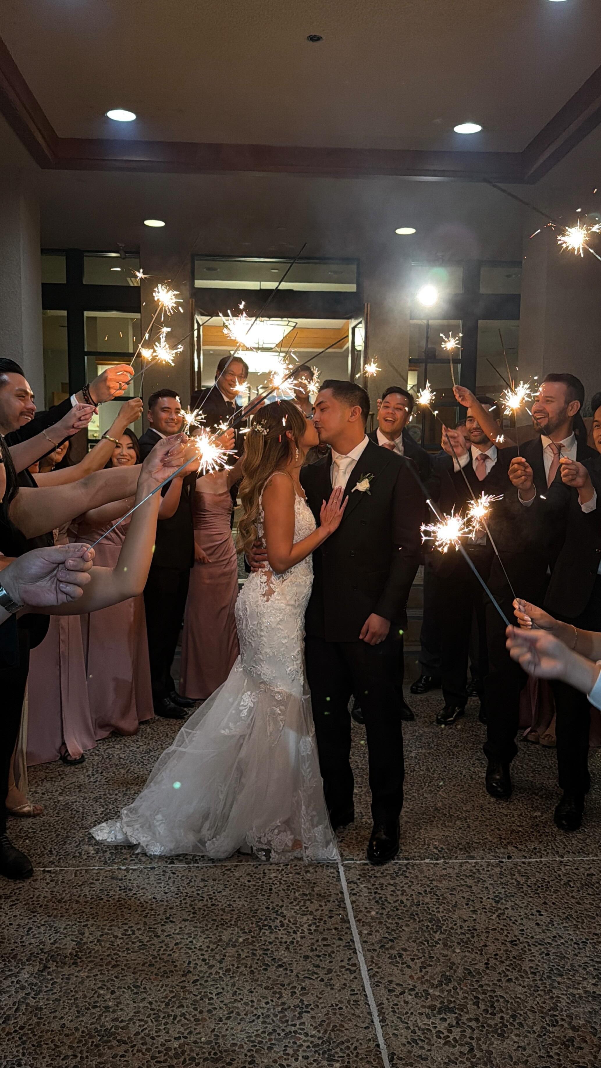 Bride and groom kissing amidst sparklers held by wedding guests.