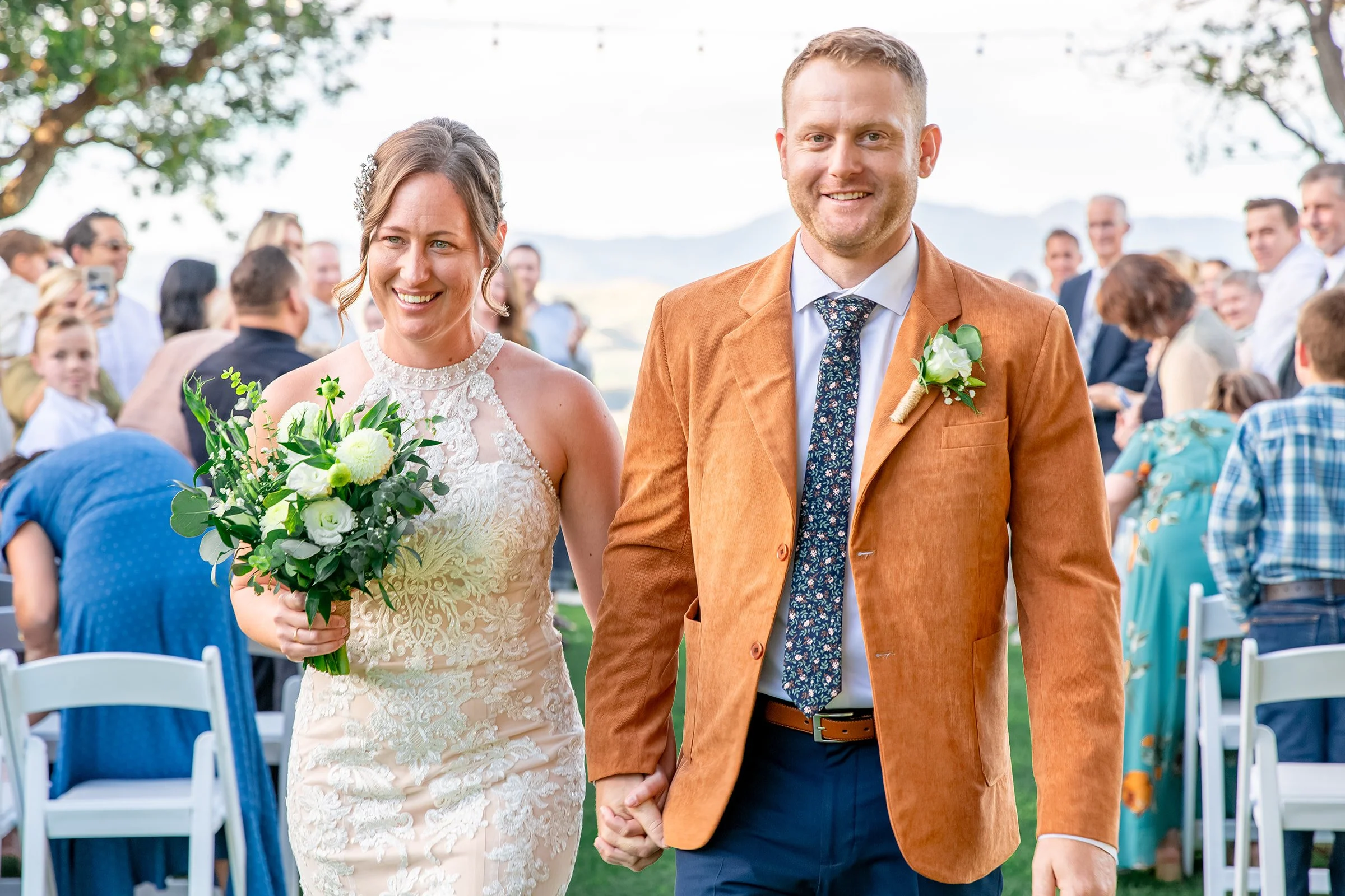 Group of wedding guests celebrating with a bride and groom in front of a rustic wall decorated with climbing vines and white flowers