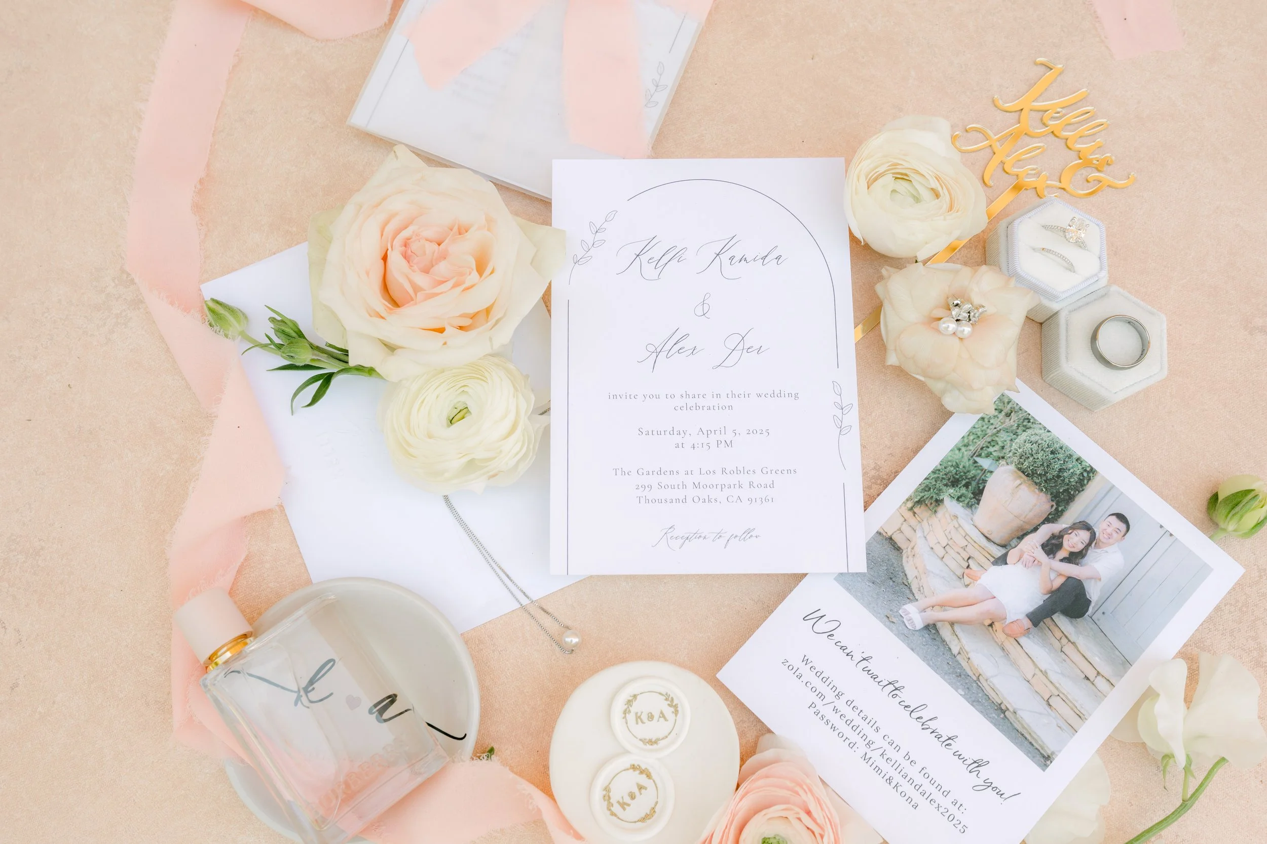 Wedding invitation, flowers, jewelry, rings, and a wedding photo arranged on a pink surface.