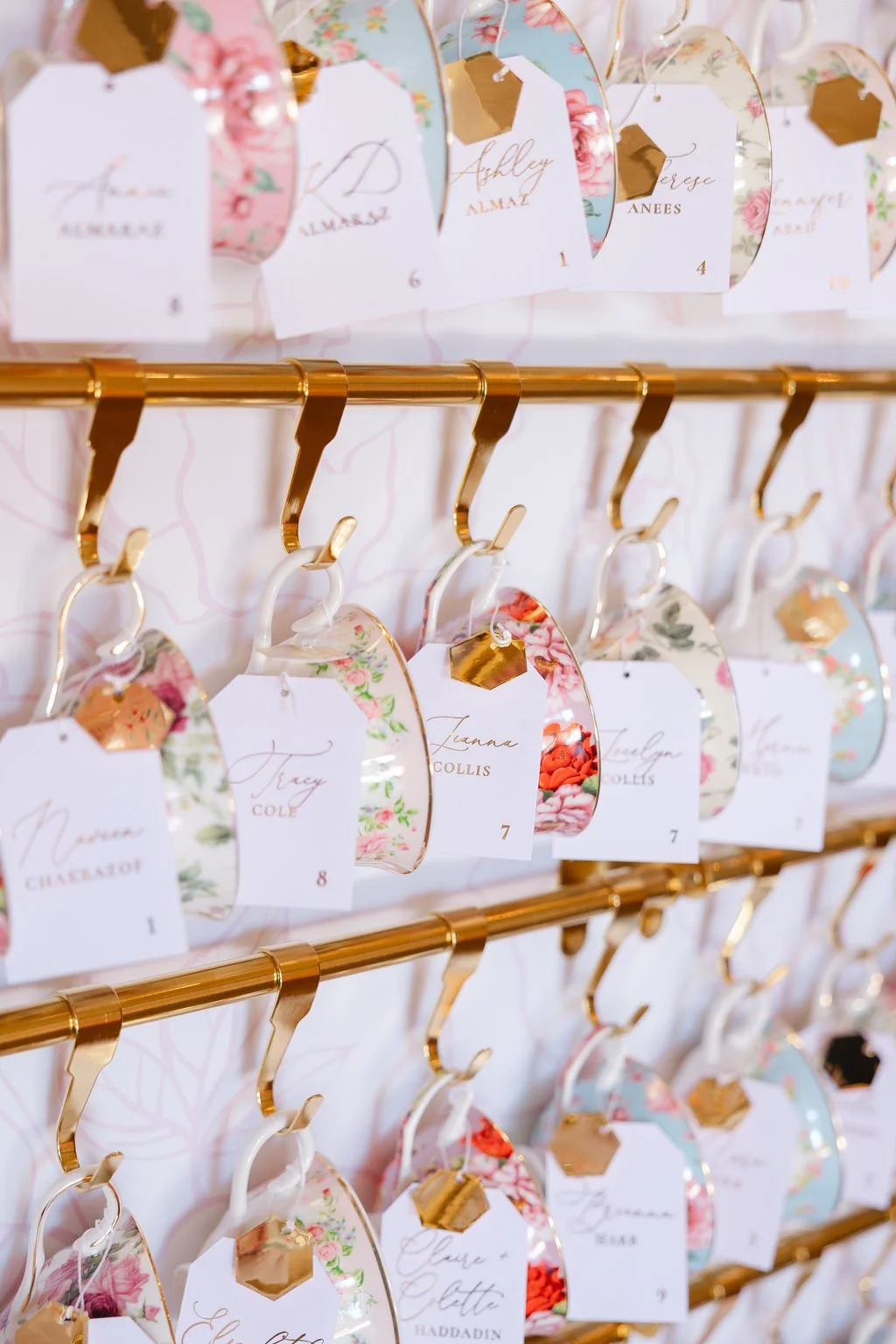 Name tags and floral decorations hanging from gold hooks on a gold display rack, likely for a wedding or event.