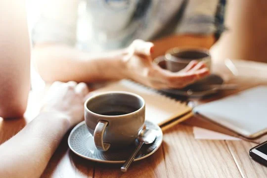 People having coffee at a wooden table with notebooks and a smartphone.