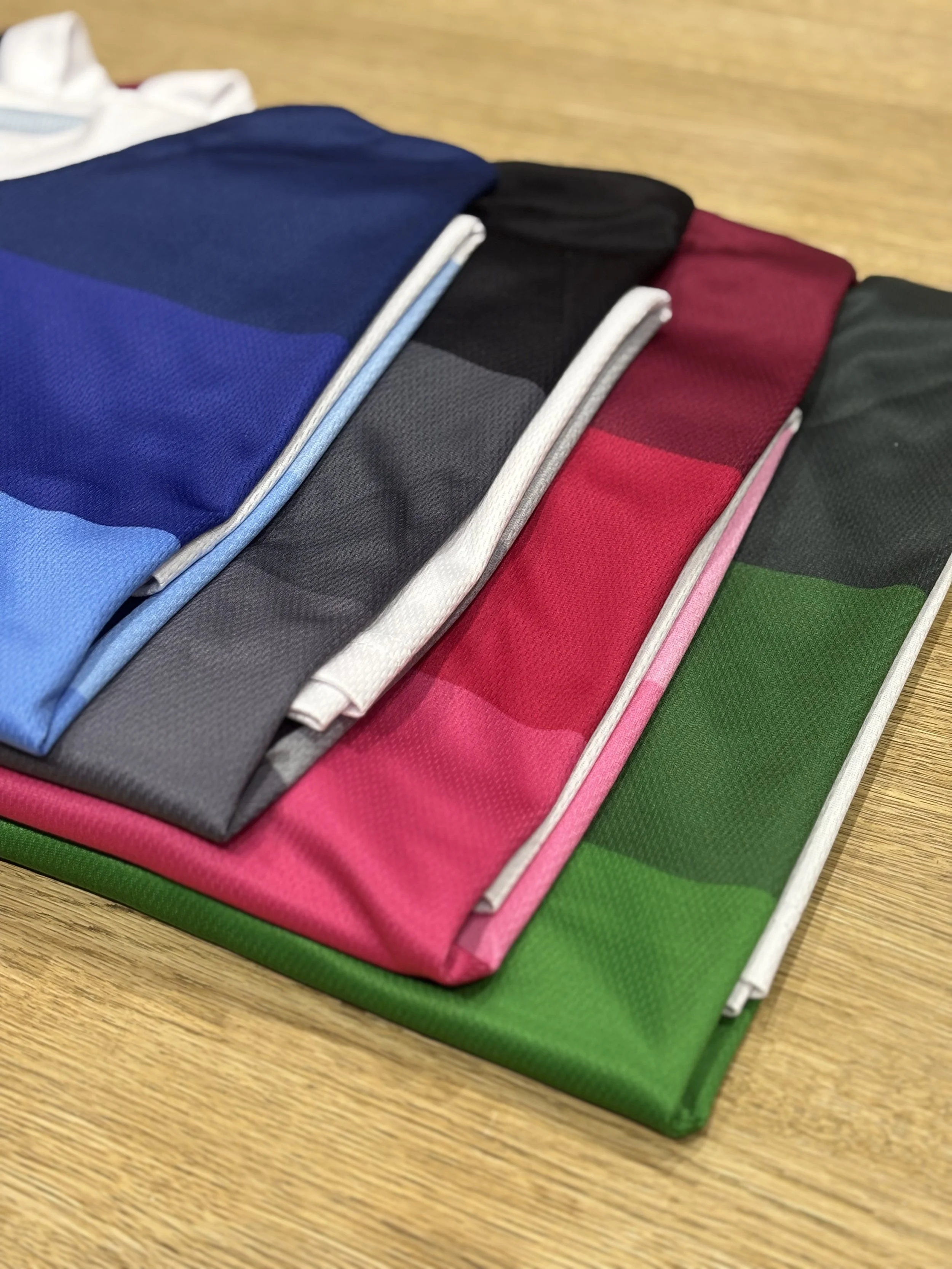 Folded colorful jackets in blue, black, gray, red, and green arranged on a wooden surface.