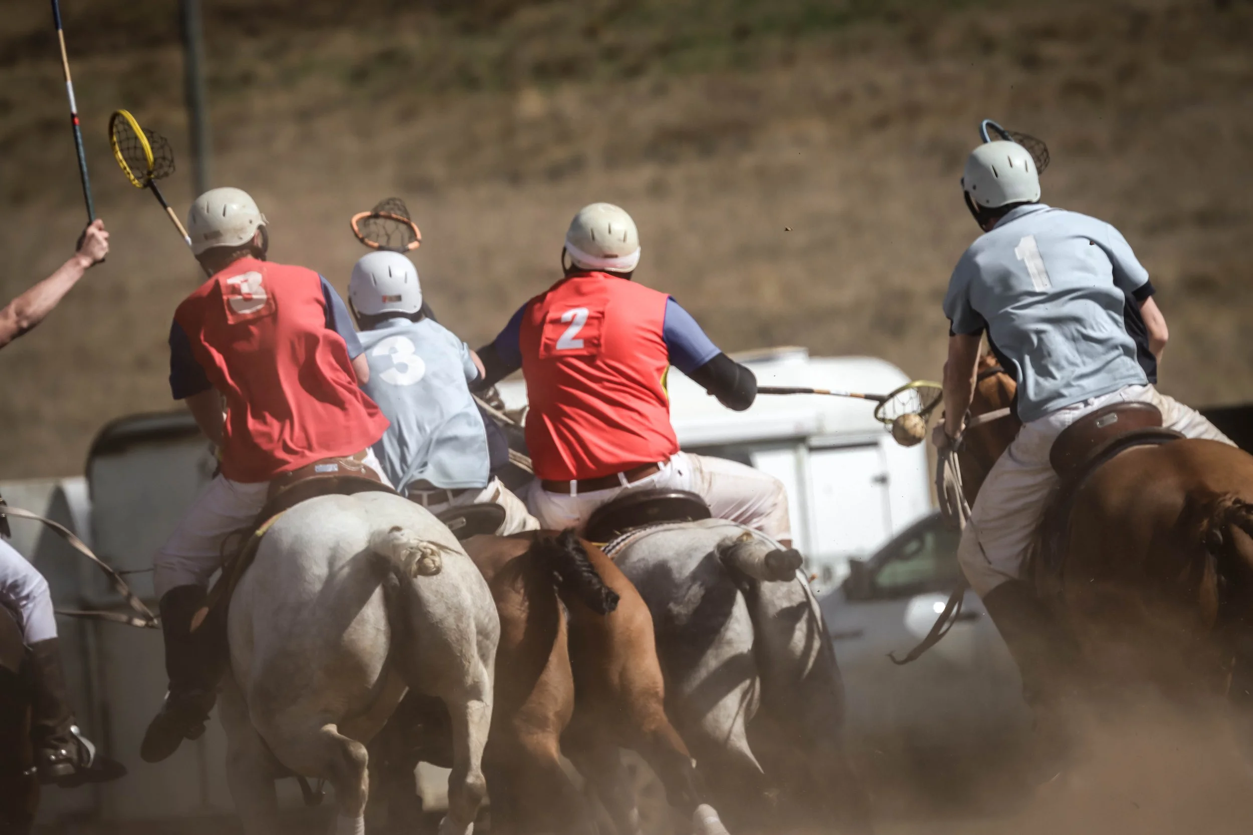 Polo players riding horses and battling with mallets during a game at an outdoor polo field.