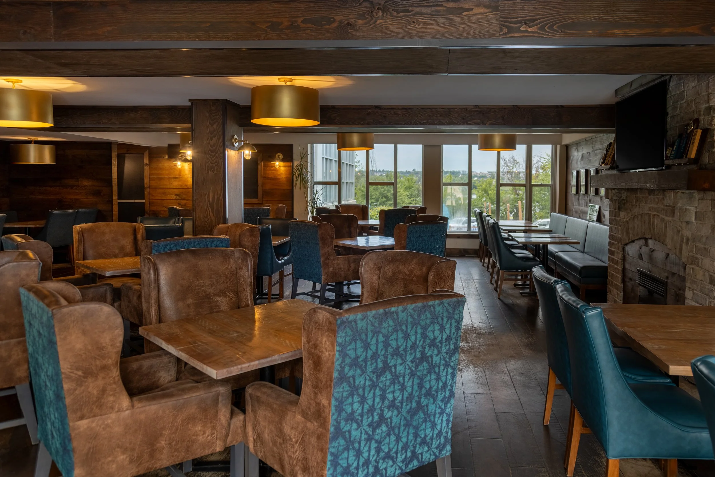 Interior of the cozy Joyce Pub with wooden walls, plush wingback leather and fabric chairs, tables, large windows with views of greenery, and warm lighting.