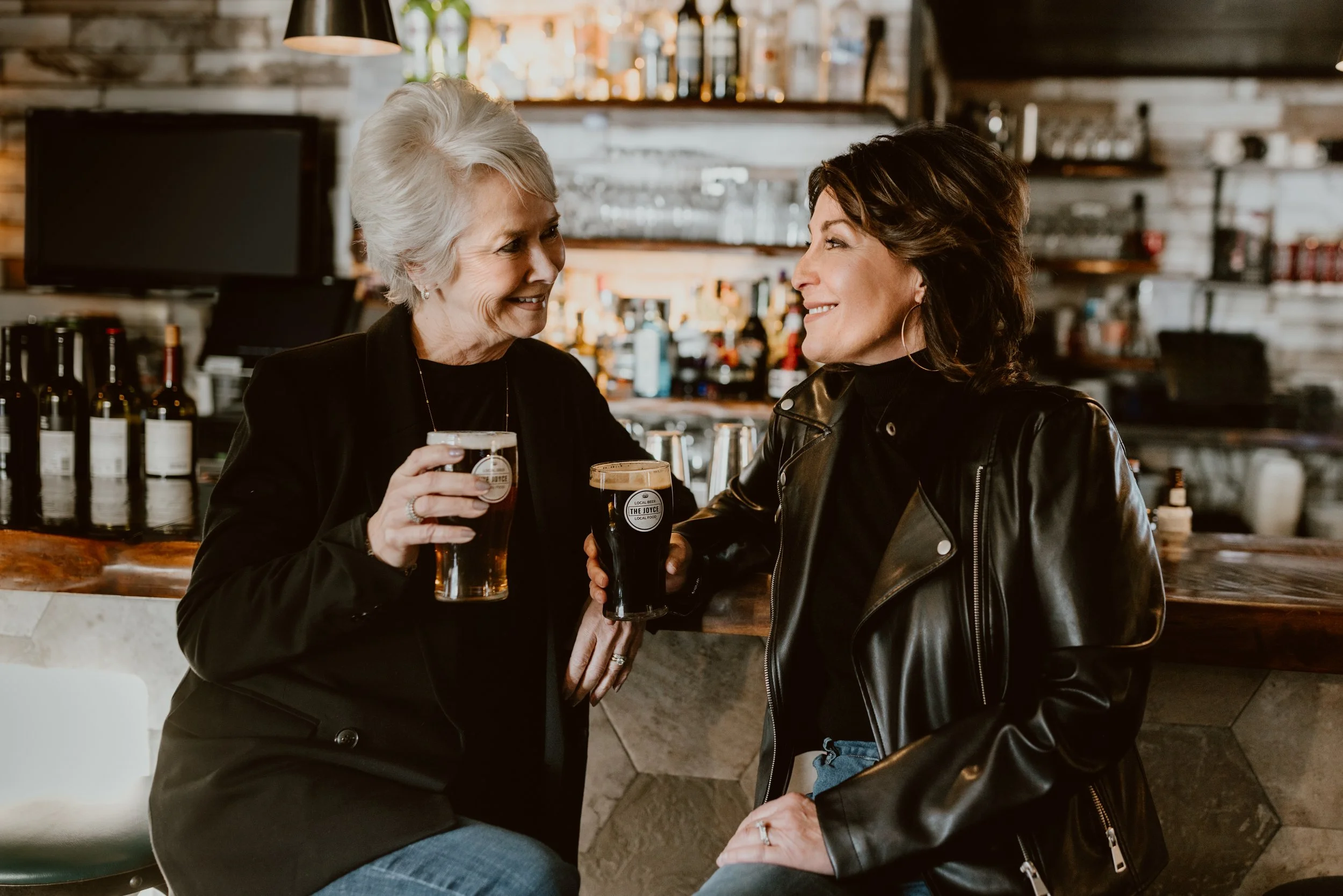 Two women enjoying drinks and smiling at each other at The Joyce bar.