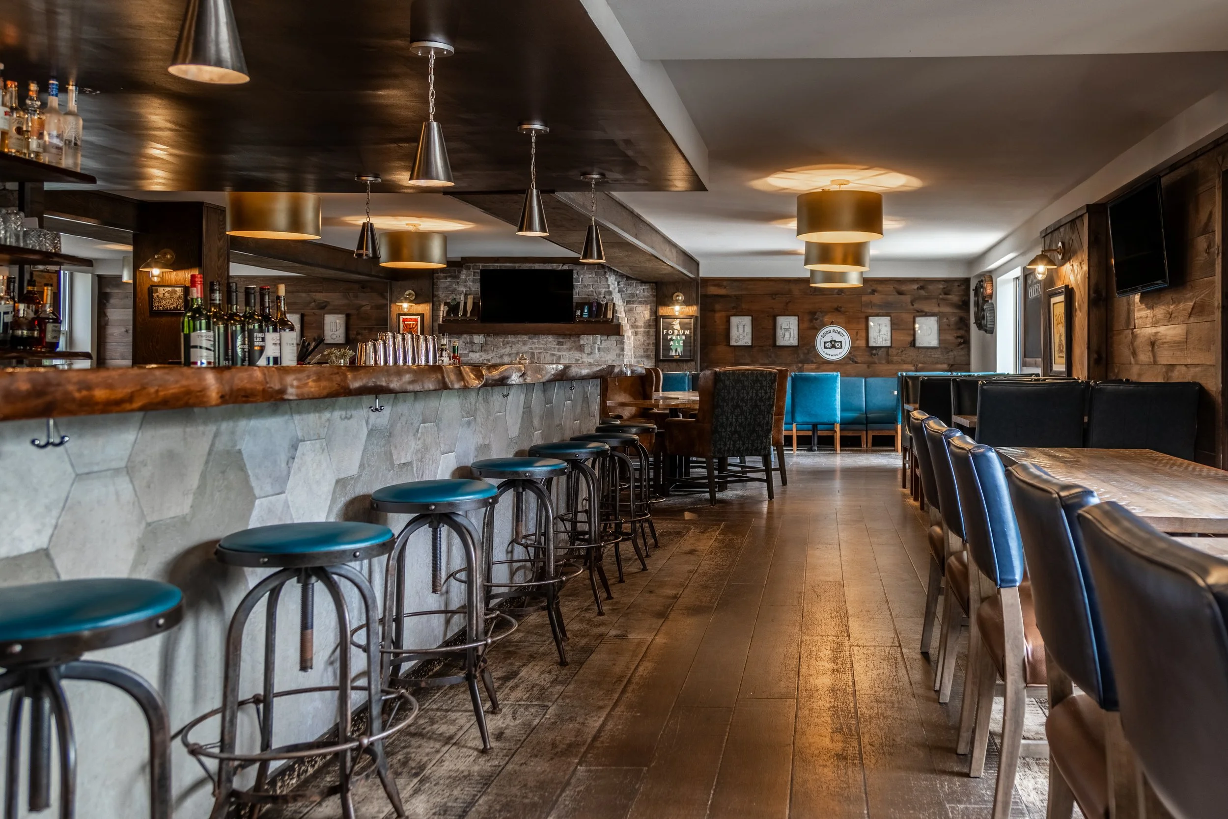 Interior of The Joyce Pub with wooden paneling, a long bar counter with bar stools, and tables with chairs. There is a TV on the wall, pendant and ceiling lights, and some wall art.
