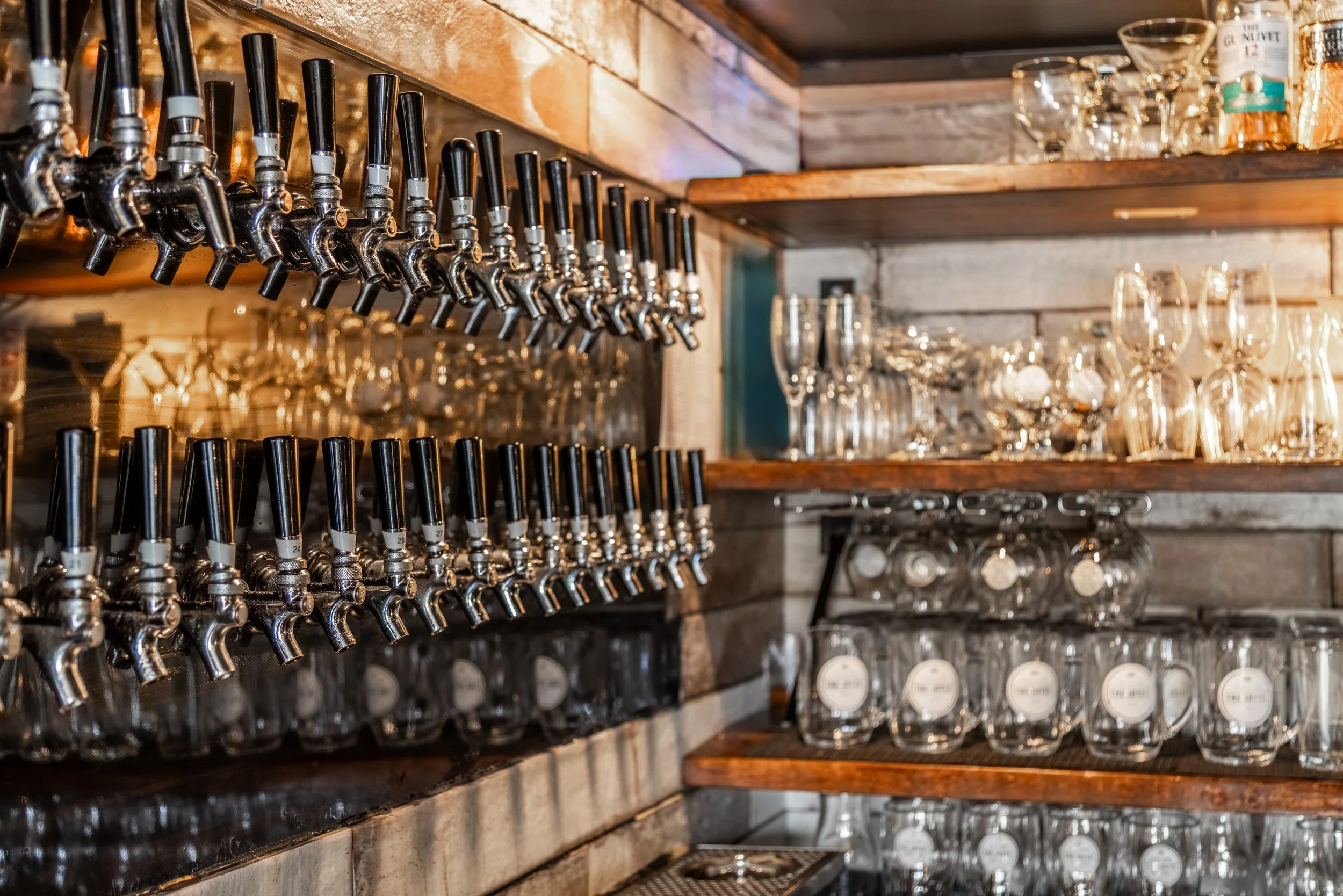Wall of craft beer taps and wood shelves with beer and wine glasses at The Joyce Pub.