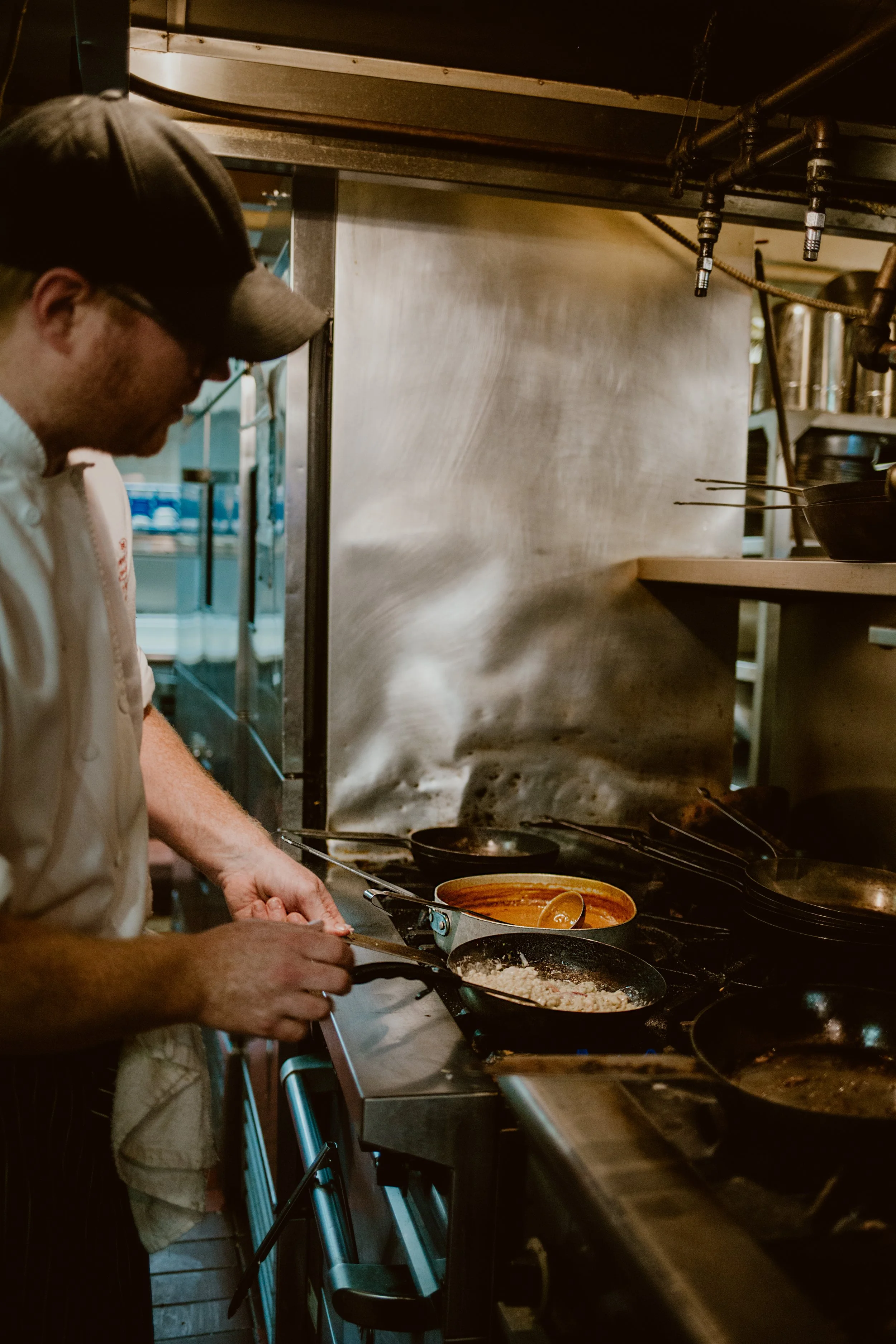 Executive chef Matt Mackenzie with glasses and a beard, wearing a white chefs jacket, working in the busy Joyce Pub kitchen.