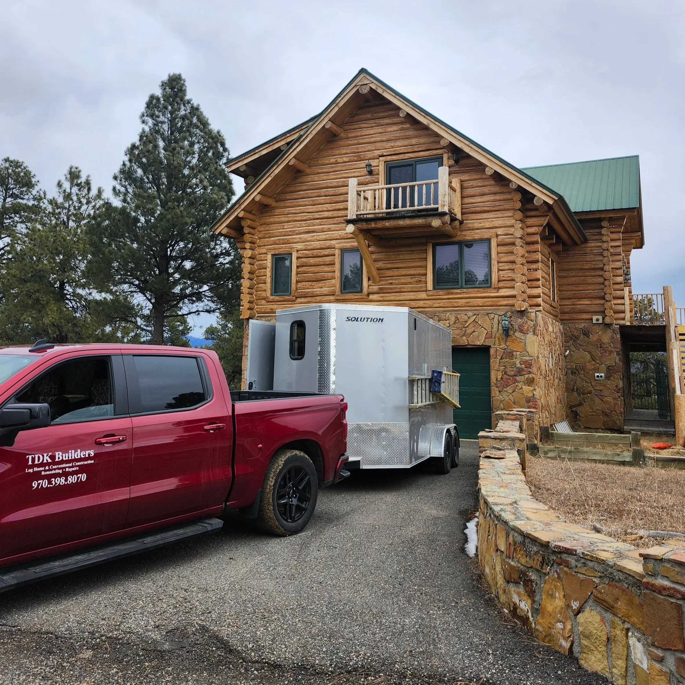 Red work truck with trailer in front of log home