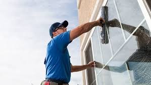 A man in a blue shirt and cap cleaning a window with a squeegee.