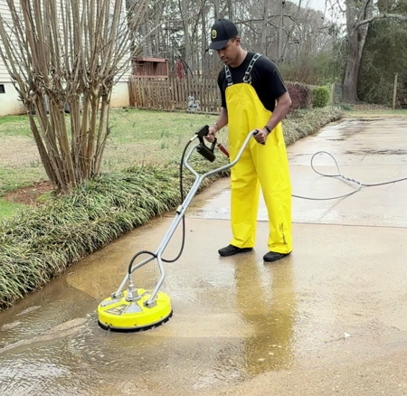 Person pressure washing a concrete driveway in front of a house.