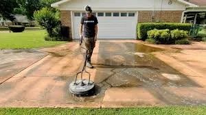 Person pressure washing a concrete driveway in front of a house.
