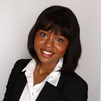 Professional woman with dark hair and a white blouse, smiling in front of a plain background.