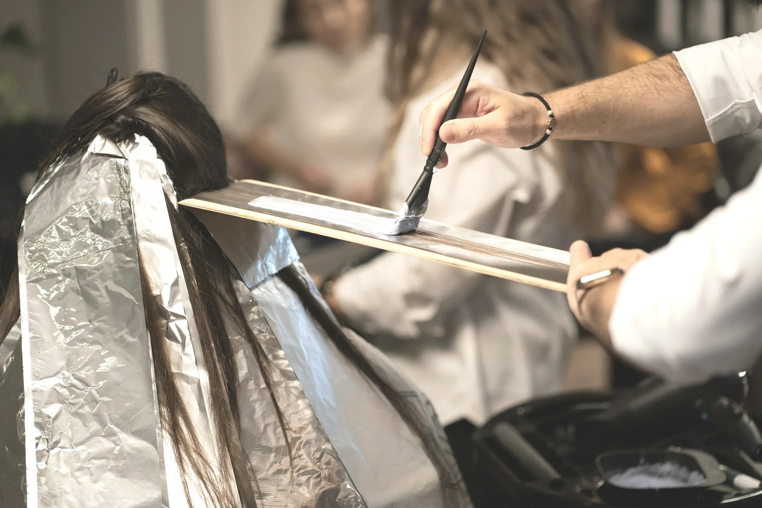 Hairdresser applying hair color or highlights to a client's hair in a salon.