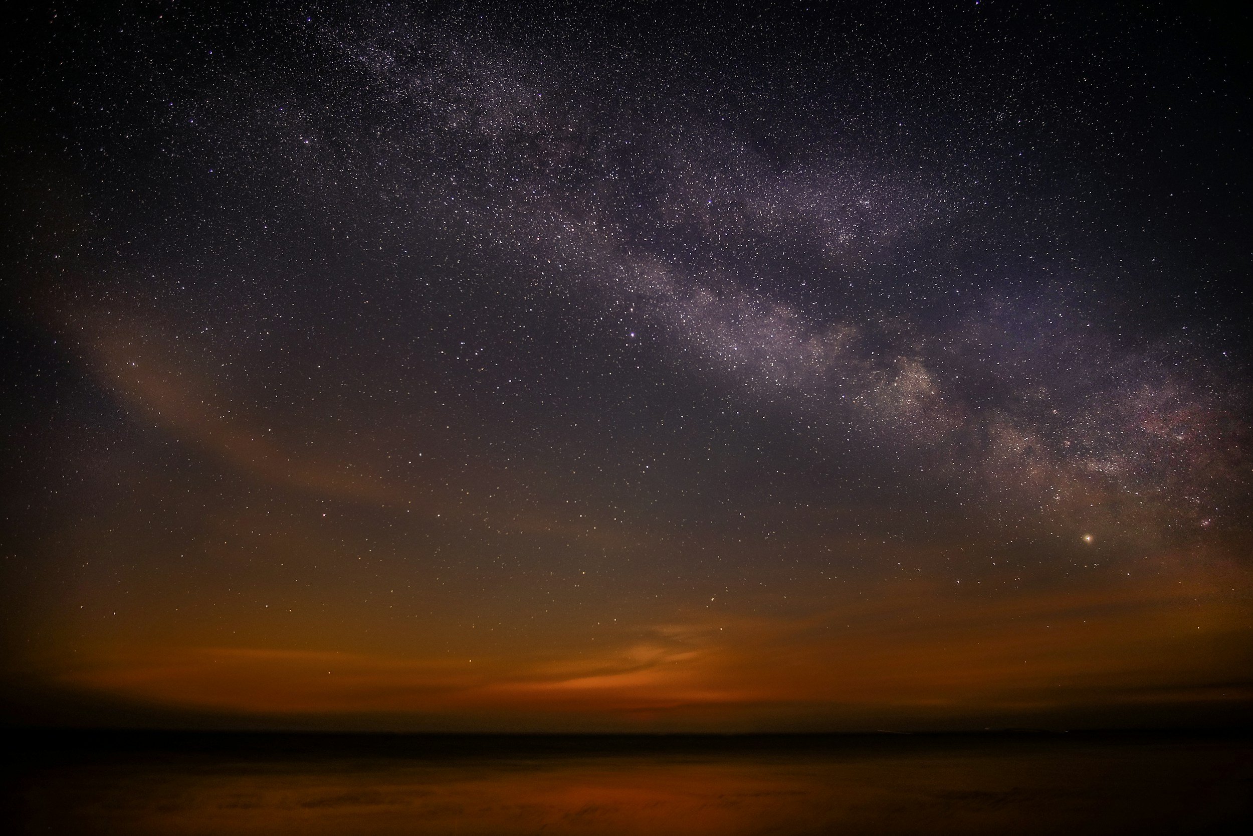 Night sky filled with stars and the Milky Way galaxy above a horizon with a faint glow.