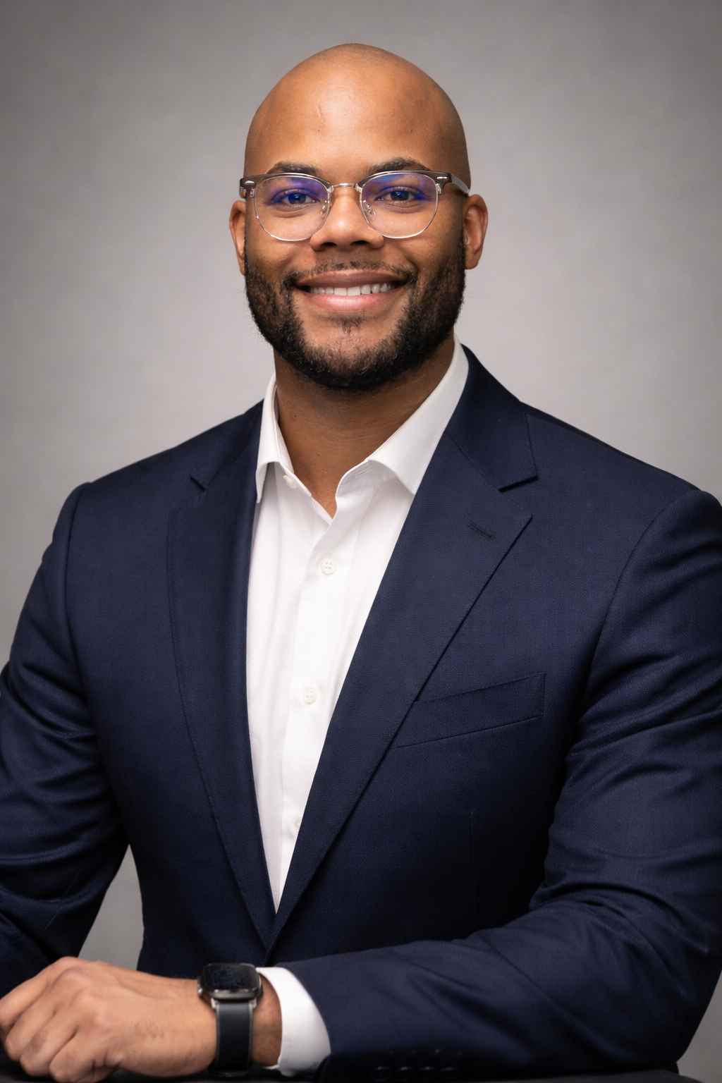 Bald black man with bead and glasses. Wearing a blue suit.