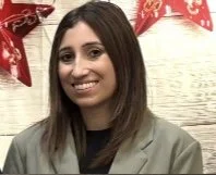 A young woman with shoulder-length brown hair smiling in front of a wall decorated with red and white banners.