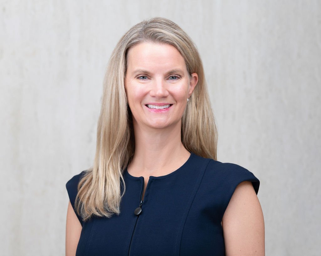 A headshot of Dr. Amy Voedisch. Dr Voedsich smiles towards the camera. She is wearing a navy blue dress and pearl earrings.