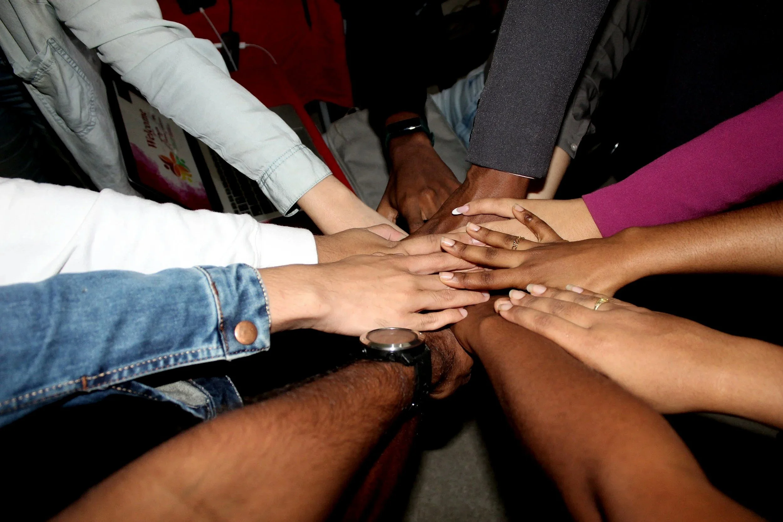 Multiple diverse hands stacked together in a gesture of teamwork or unity.