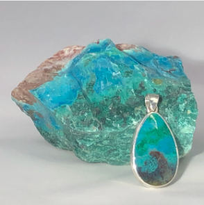 A decorative pendant featuring a colorful, abstract design hanging in front of a large, rough turquoise stone.