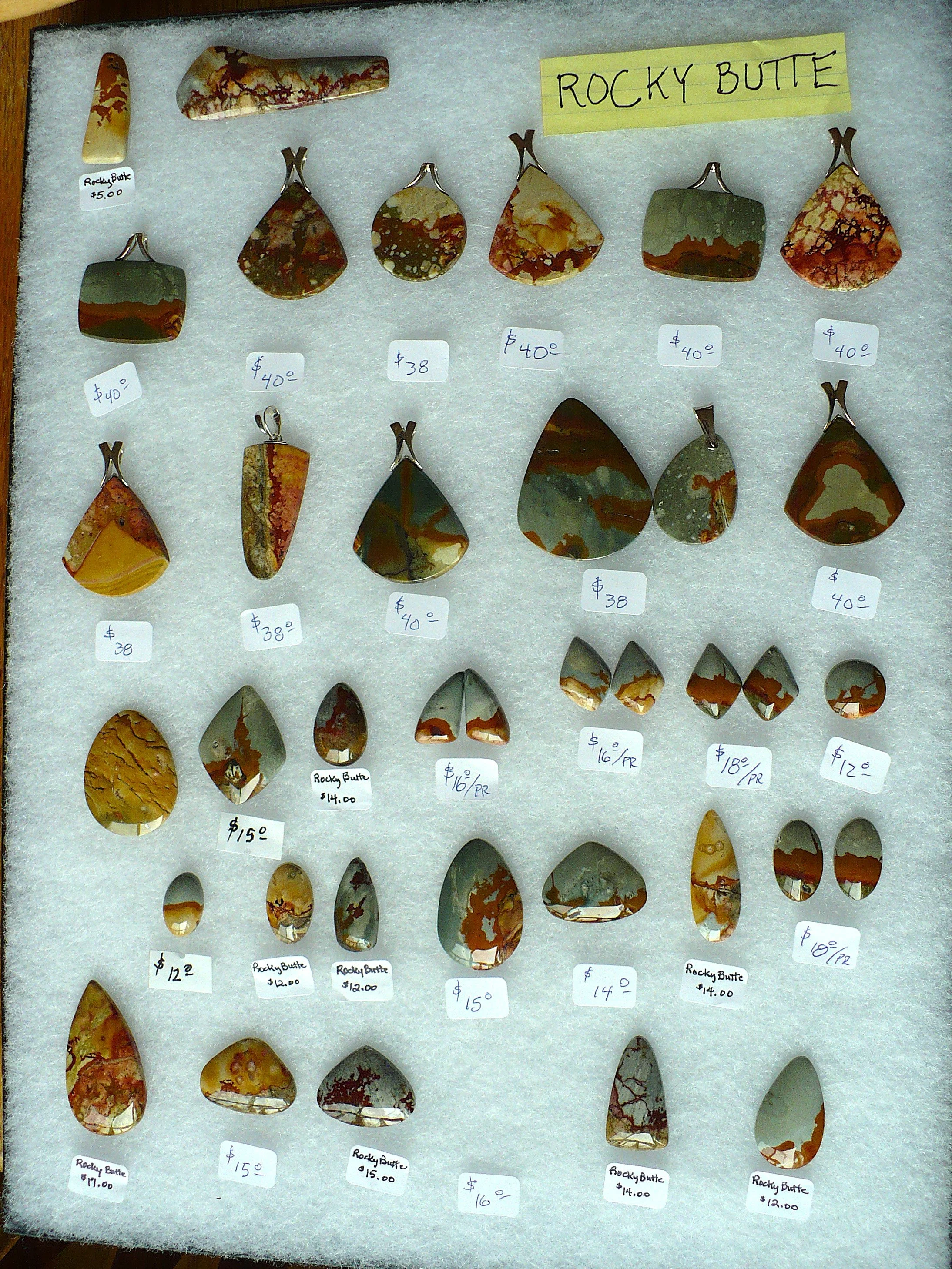 Display of various polished stones and pendants from Rocky Butte, each with price tags. The stones are multicolored with patterns of reds, greens, browns, and yellows, and some are labeled with prices such as $40, $38, $15, and $12.