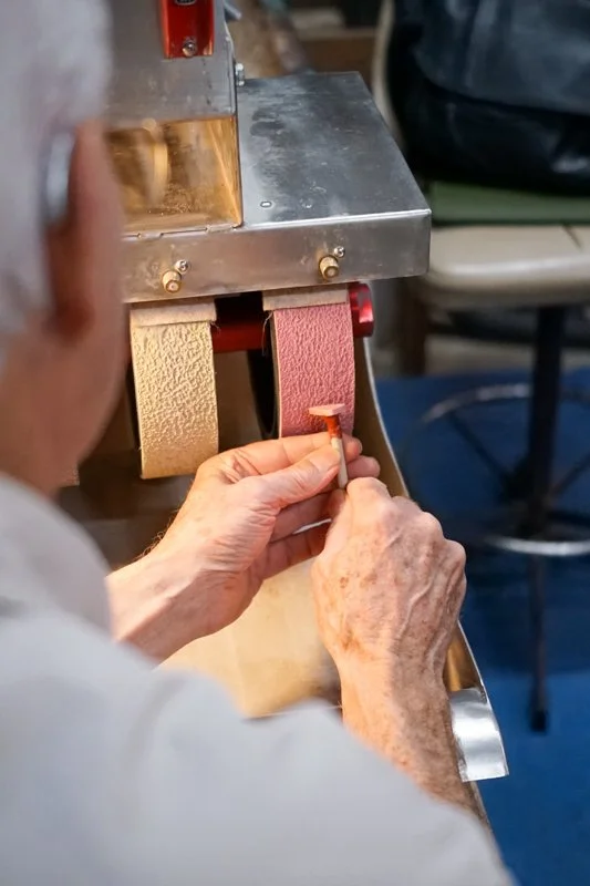 A person using a machine to make leather belts, with strips of leather in gold and red being processed.