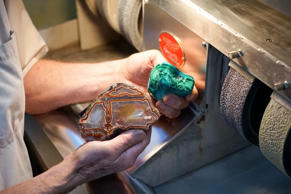 Person polishing a semi-precious stone on a machine with grinding wheels.