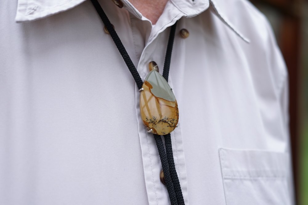 A man wearing a white collared shirt with a decorative pendant on a black cord around his neck.