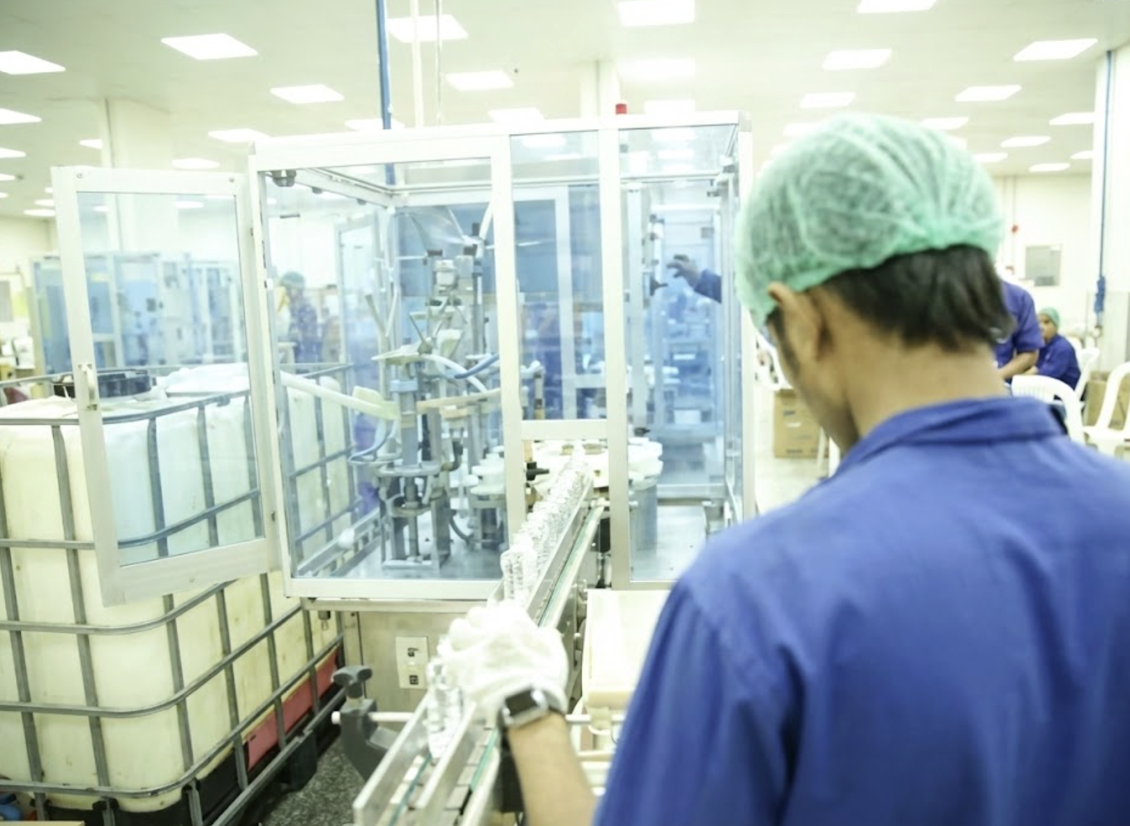 A worker in a blue uniform and green hairnet operating machinery in a manufacturing or pharmaceutical facility. مصنع عبد الصمد القرشي