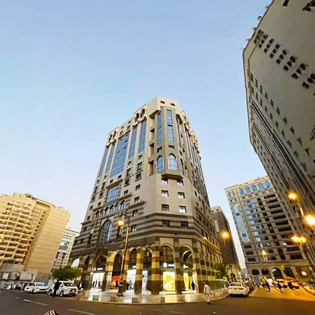Dar Al-Andalus Hotel in Al-Madinah, tall modern building with arched windows and a beige facade, surrounded by other high-rise buildings in an urban setting at dusk. فندق دار الأندلس في المدينة