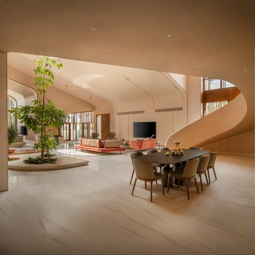 Spacious, modern living room and dining area with curved architecture, a large television, a central tree, and contemporary furniture, including a black dining table and beige chairs. تصميم داخلي مميز وتشطيبات رائعة في جدة