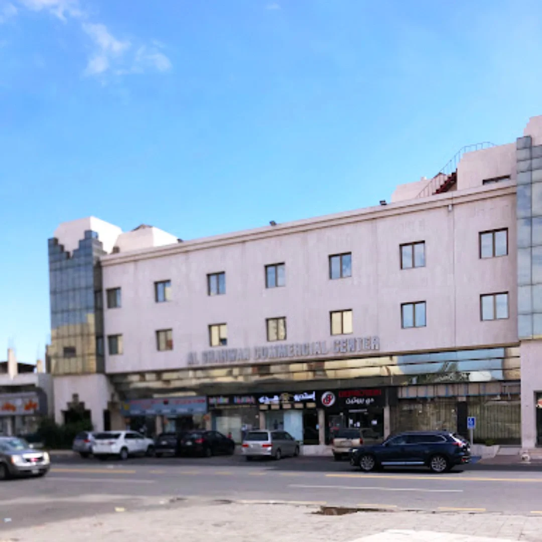 Exterior view of the Al Regional Dentalial Center building with parked cars in front and storefronts on the ground level under a clear blue sky. Shahawan Center. مركز الشهوان في جدة حي الحمراء
