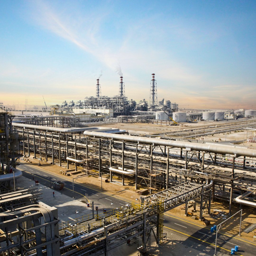 Rabigh power plant in saudi arabia. Industrial oil refinery with pipelines, storage tanks, and smokestacks emitting smoke under a blue sky. محطة كهرباء رابغ