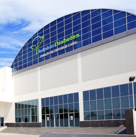 Exterior of a medical facility with a sign for Julphar Diabetes, Outpatient Accessible Care, on a partly cloudy day. مصنع جلفار للادوية